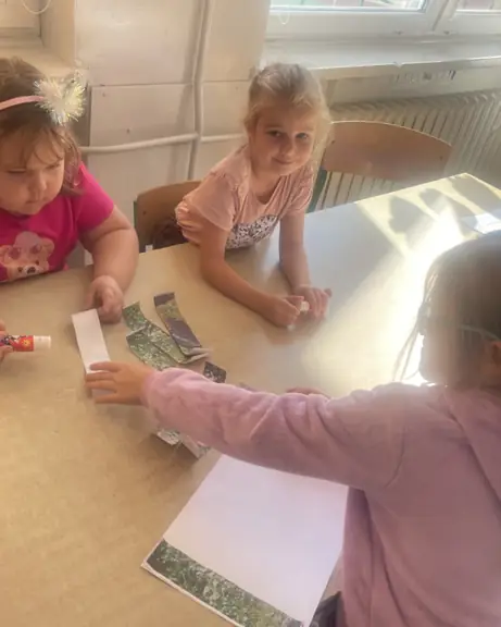 Trzy dziewczynki przyklejają papierowe puzzle na kartkę.