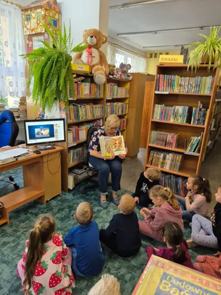 Dzieci z grupy 01 oglądają ilustracje książki czytanej przez panią bibliotekarkę.