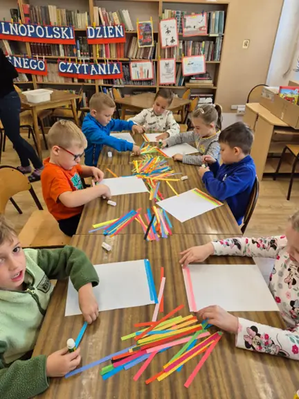 Dzieci z grupy Kotki przyklejają kolorowe paski papieru.