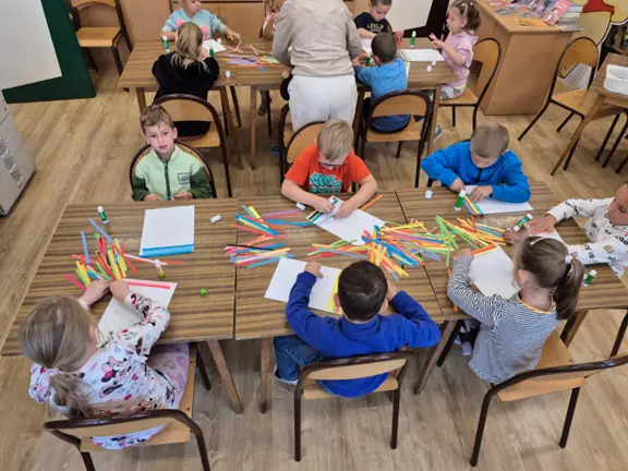 Przedszkolaki z grupy Kotki przyklejają kolorowe paski papieru.