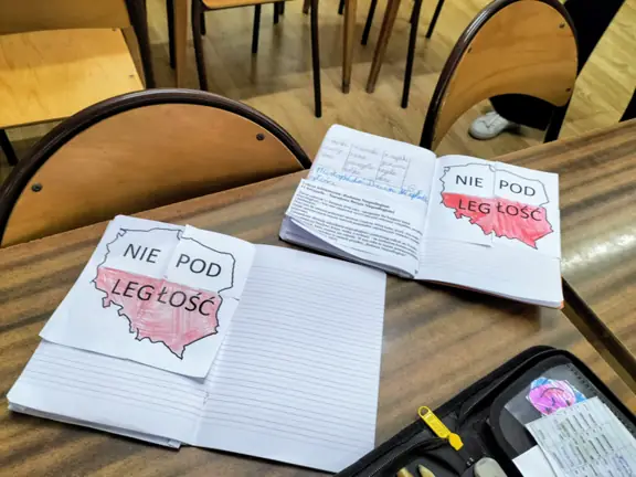 Zdjęcie przedstawia zeszyty ucznów z wklejoną informacją o Święcie Niepodległości oraz mapą Polski ułożoną z puzzli.