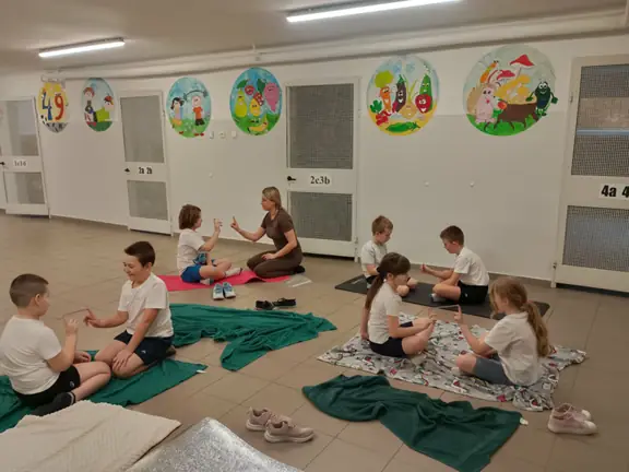 grupa-uczniow-siedzi-na-matach-i-kocach-i-wykonuje-cwiczenie-ze-slomka-jpg