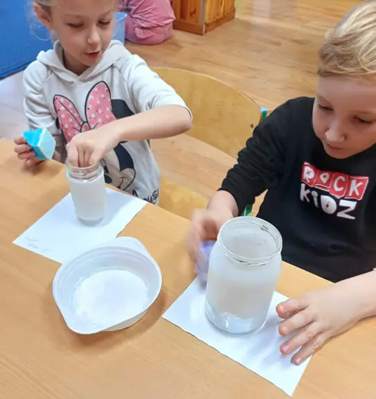 uczniowie malują słoiki na biało za pomocą gąbki