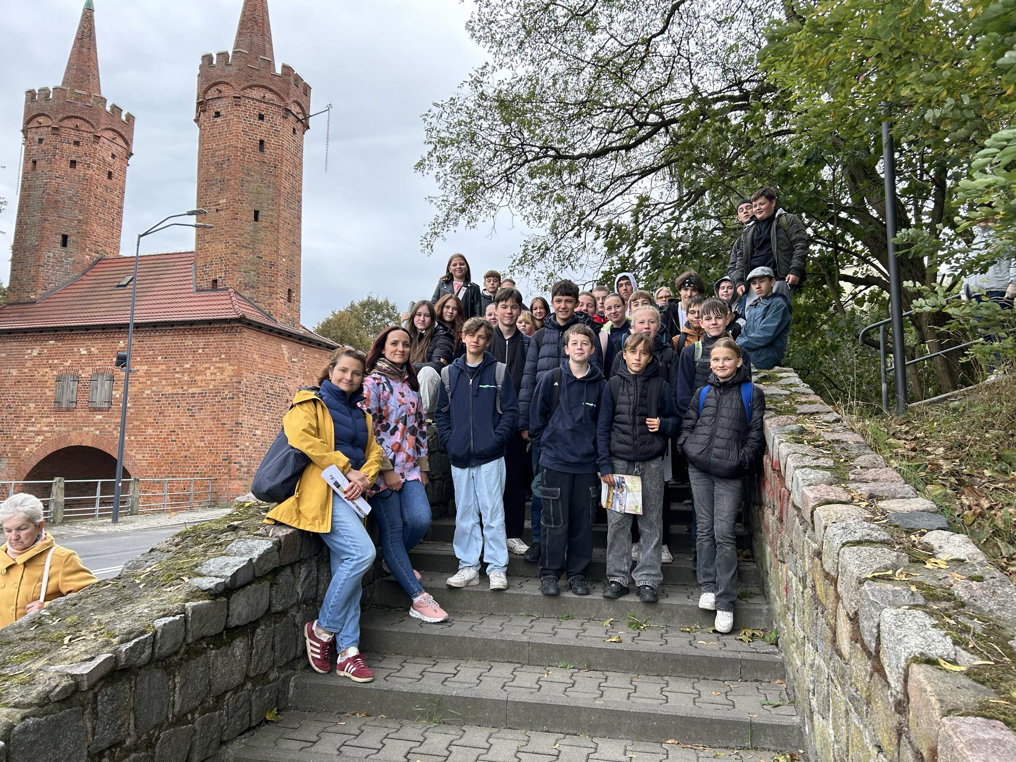 grupa uczniów ze Stargardu i Eberswalde pozuje do zdjęcia na schodach, a w tle widać Bramę Portową. 