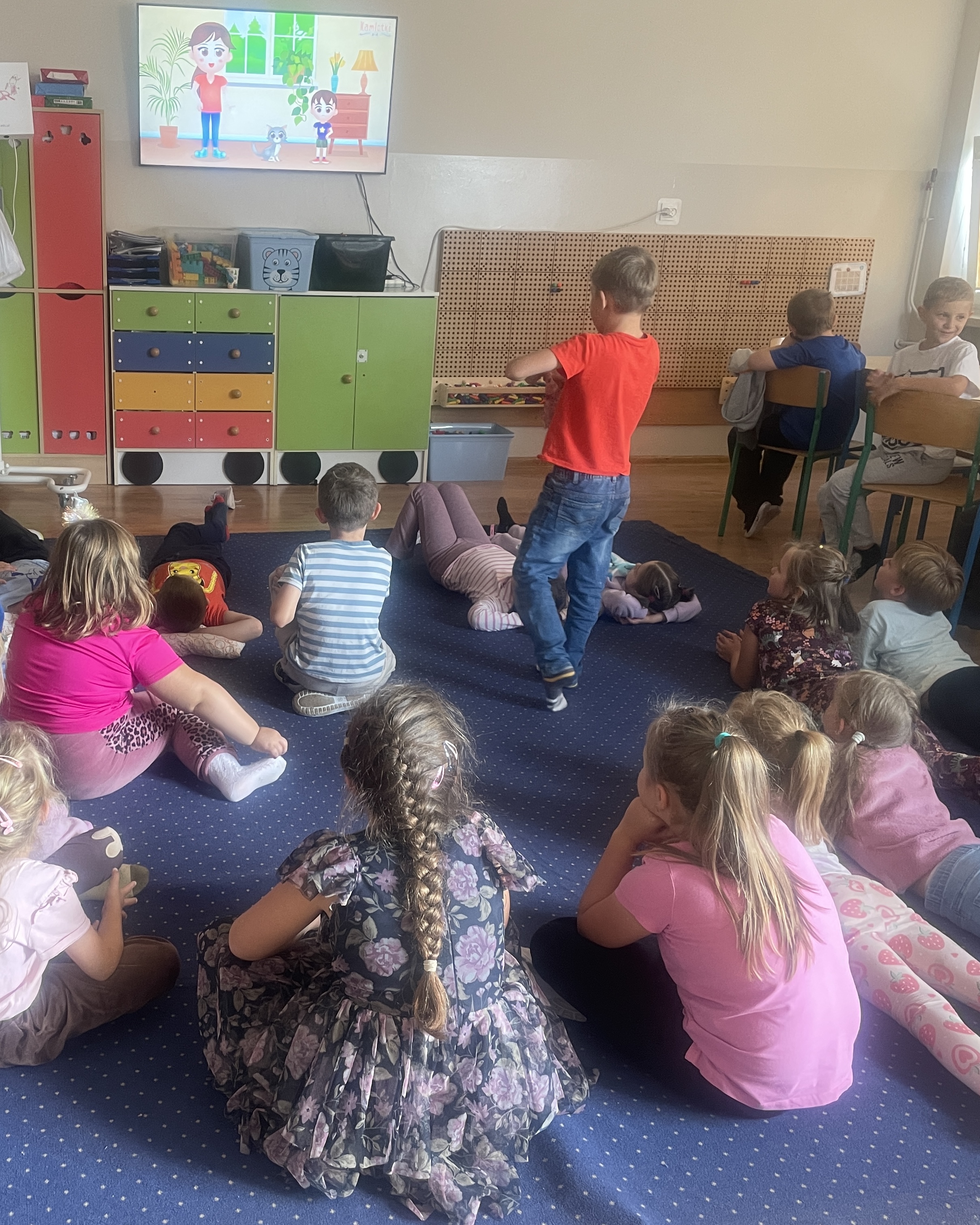 Grupa dzieci na dywanie i przy stoliku oglądająca edukacyjny filmik nt